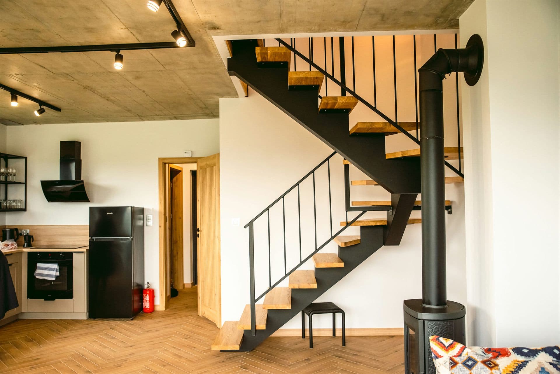 Salon z czarnymi schodami, otwartą kuchnią i piecem
